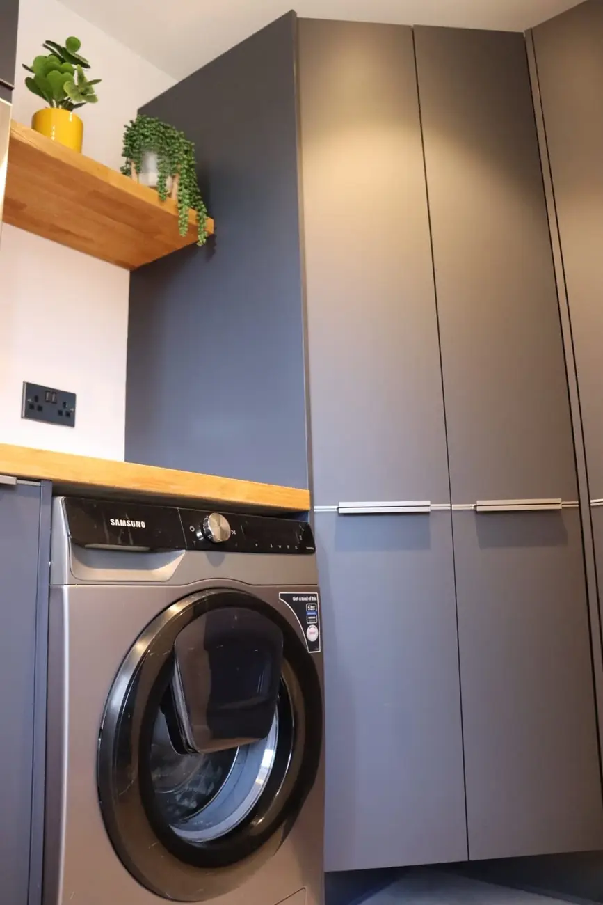 Utility room with washing machine, dark cabinetry and open oak shelving